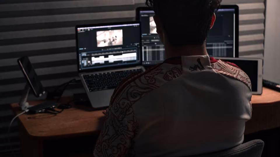 Monteur face à un portable et un écran affichant une timeline vidéo.