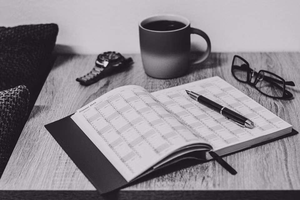 Agenda ouvert, stylo, lunettes et café en noir et blanc.