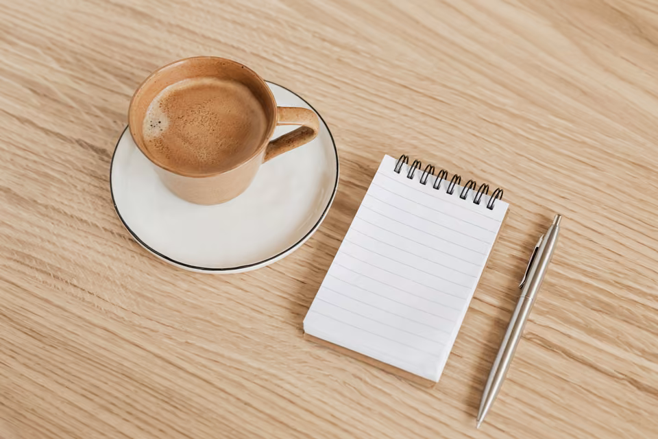 Carnet vierge et stylo près d’un café sur une table en bois.