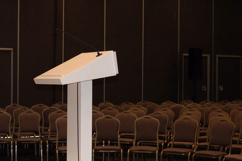 Pupitre blanc devant les rangées de chaises d’une salle de conférence.