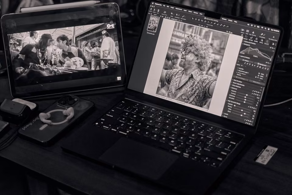 Photo en noir et blanc d’un portable affichant les réglages de retouche d’un portrait près d’une tablette.