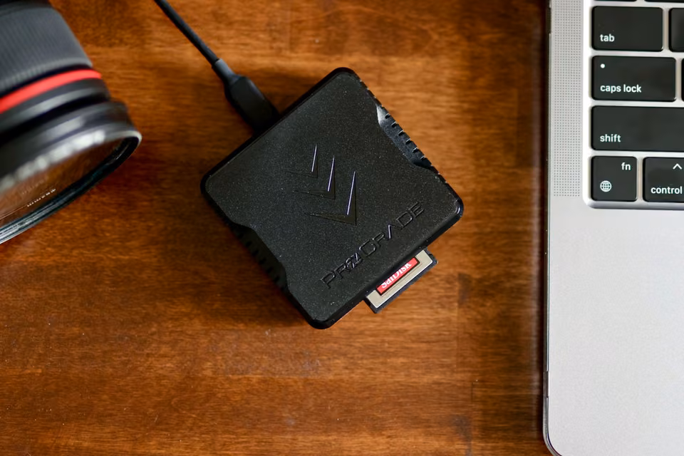 Lecteur de cartes mémoire branché près d’un portable et d’un objectif photo.