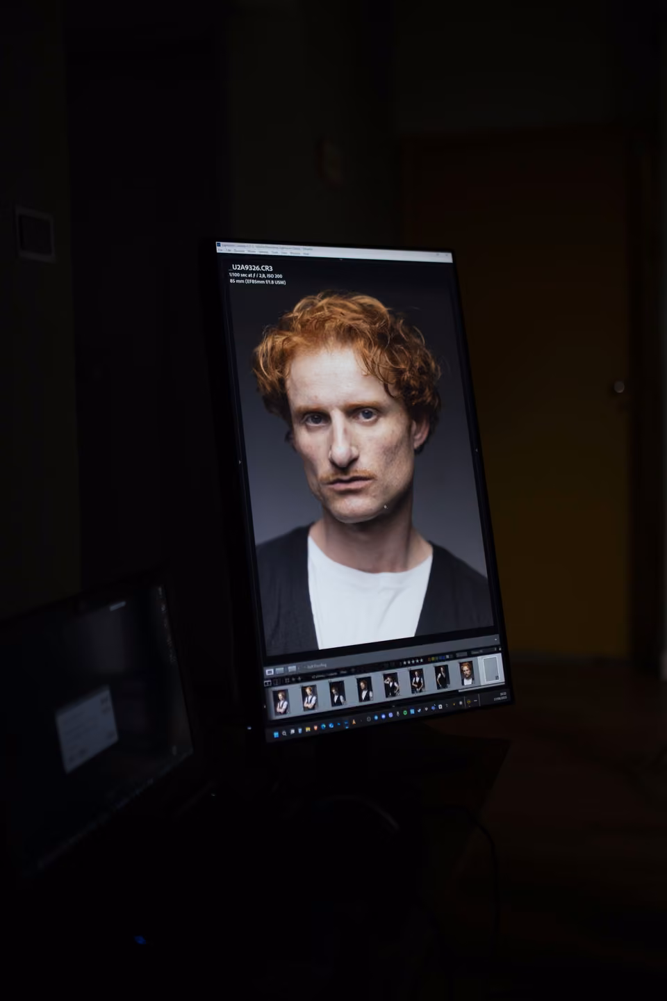 Portrait photographique en cours de retouche sur un écran vertical dans un studio sombre.