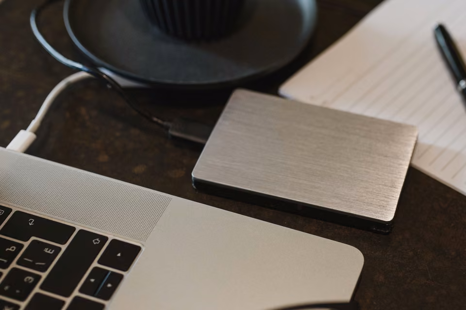Disque externe métallique branché près d’un portable et d’un carnet.